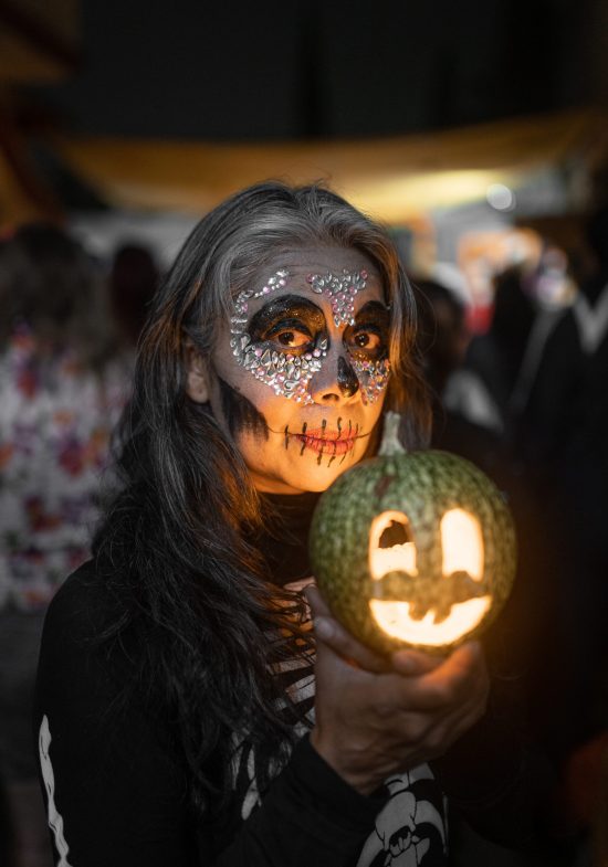 An adult Hispanic woman is posing with a lighten gourd during Day of the Dead celebration. Concept of traditional Dia de Muertos in Mexico