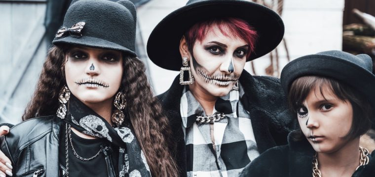 Scary family, mother, daughters celebrating halloween. Terrifying black, white skull half-face makeup and witch costumes, stylish images. Horror,fun at children's party in barn on street.Hats,jackets.